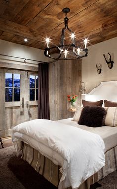 a large bed sitting under a chandelier next to a wooden ceiling in a bedroom