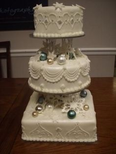 three tiered wedding cake with white frosting and pearls on top sitting on a wooden table