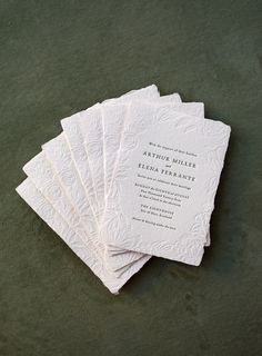 five white wedding cards sitting on top of a green cloth covered table next to each other