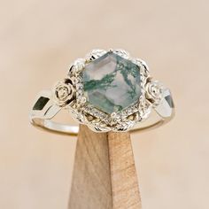 a green and white ring sitting on top of a wooden stand with a diamond in the center