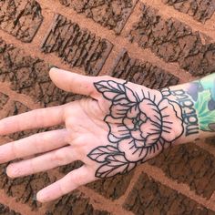 a person's hand with a flower tattoo on it, next to a brick wall