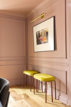 two yellow stools in front of a pink wall with a framed photograph on it