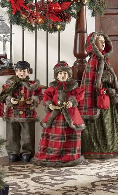 three dolls are dressed in red and green plaid outfits, standing next to a christmas tree