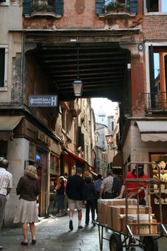 people are walking down an alley way with carts on the sidewalk and buildings in the background