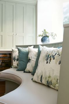 a white bench with pillows on it and a vase full of flowers in the background