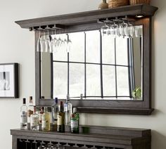 a bar with wine glasses and bottles on it in front of a mirror that is hung above the counter