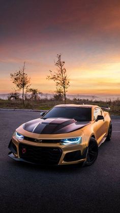 a gold chevrolet camaro is parked on the side of the road in front of an orange sunset