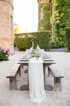 a table set up with white linens and flowers on it in front of a building