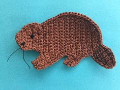 a crocheted beaver brooch with a needle in it's mouth on a blue background