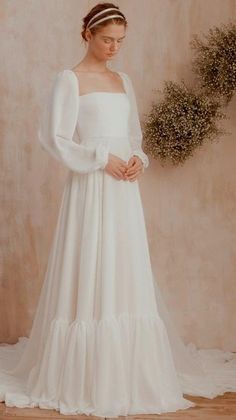 a woman in a white wedding dress standing next to a wall with a wreath on it