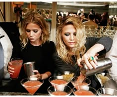 two women at a bar pouring drinks into cocktail glasses with another woman in the background