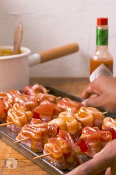 two hands holding skewers of food on a metal tray with ketchup