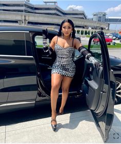 a woman in a short dress stepping out of a black car with her hand on the door handle