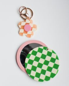 two keychains are sitting next to each other on a white surface, one has a green and pink checkerboard design