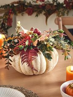 a table topped with white pumpkins filled with flowers and greenery next to candles