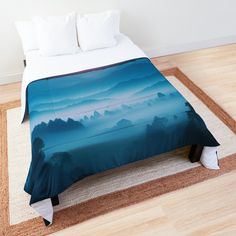 a bed covered in a blue blanket on top of a wooden floor next to a rug