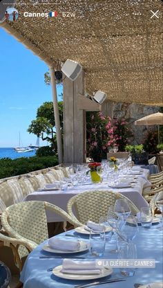 an outdoor dining area with white table cloths and chairs, overlooking the ocean on a sunny day