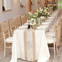 a long table is set with white flowers and place settings for the guests to sit at