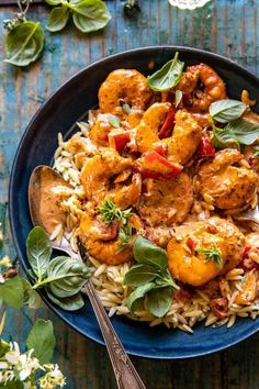 a blue plate filled with pasta and shrimp on top of a wooden table next to silverware