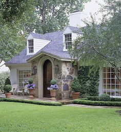 a small house with lots of windows and plants in the front yard, surrounded by greenery