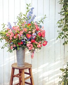 a metal vase filled with pink and blue flowers on top of a wooden stool next to a white wall