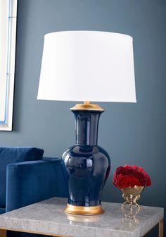 a blue vase with red flowers on a table next to a lamp and couch in a living room