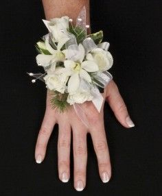 a woman's hand with white flowers and greenery on her wrist, against a black background