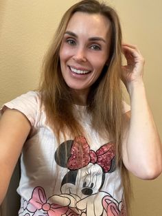 a woman with long hair wearing a minnie mouse t - shirt smiles at the camera