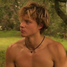 a shirtless young man with no shirt on standing in front of some trees and grass