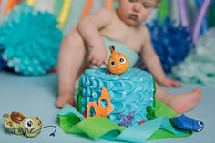 a baby sitting on the floor next to a cake with a fish decoration on it