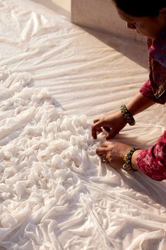 a woman is laying on the ground with her hands together and sewing something white fabric