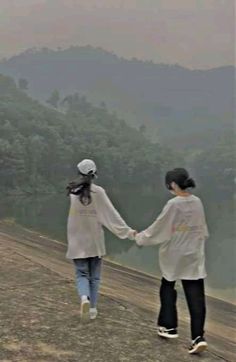 two people holding hands while walking on the side of a hill with trees in the background