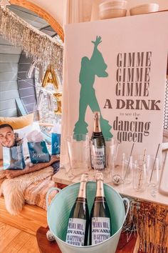 two bottles of champagne are sitting in a bucket on the floor next to a sign that says gimme gimme, a drink and a dancing queen