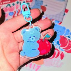 a hand holding a keychain with a bear and an apple on the front