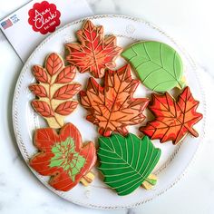 decorated leaf cookies on a white plate with red, green and orange leaves in the background