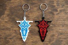 two keychains with different designs on them sitting on a wooden surface, one is blue and the other is red