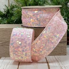 two rolls of pink sequinized ribbon on wooden boards with pine branches in the background