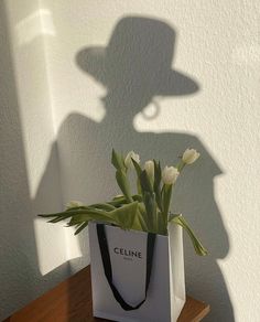 a white bag with flowers in it sitting on a wooden table next to a wall