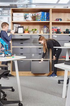 two children are playing with toys in an office setting, one is pushing the drawer open