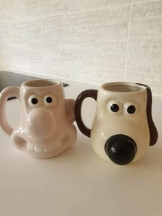 two coffee mugs with faces on them sitting on a counter