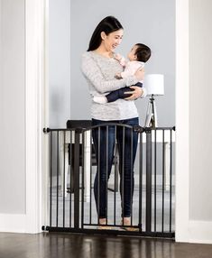 a woman holding a baby in her arms and standing next to a black metal gate