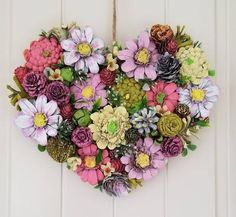 a heart - shaped wreath made out of flowers hangs on a white door with rope