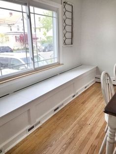 a dining room table with chairs and a bench in front of a large window overlooking the street