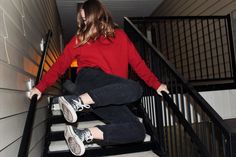 a woman in red sweater and black jeans walking down stairs with white sneakers on her feet