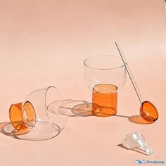 three glasses with orange liquid and one filled with ice cubes on a pink background