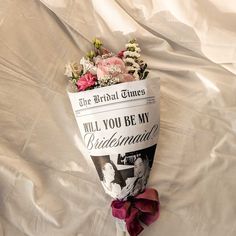 a bouquet of flowers sitting on top of a white sheet covered bed next to a newspaper