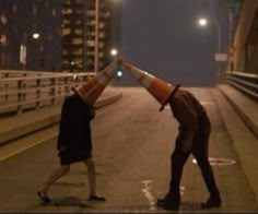 two people standing on the side of a road with traffic cones over their heads,