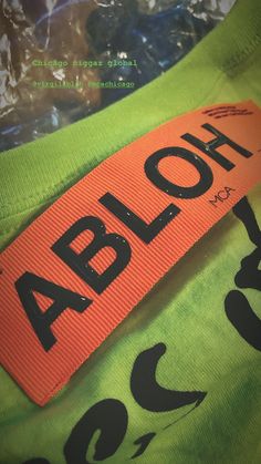 an orange and black label on a green shirt that says abloh in large letters