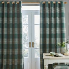 a bedroom with green plaid curtains and a white table in front of the door that is open