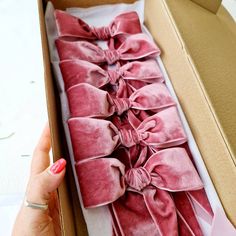 a woman's hand is holding an open box with pink velvet bows on it